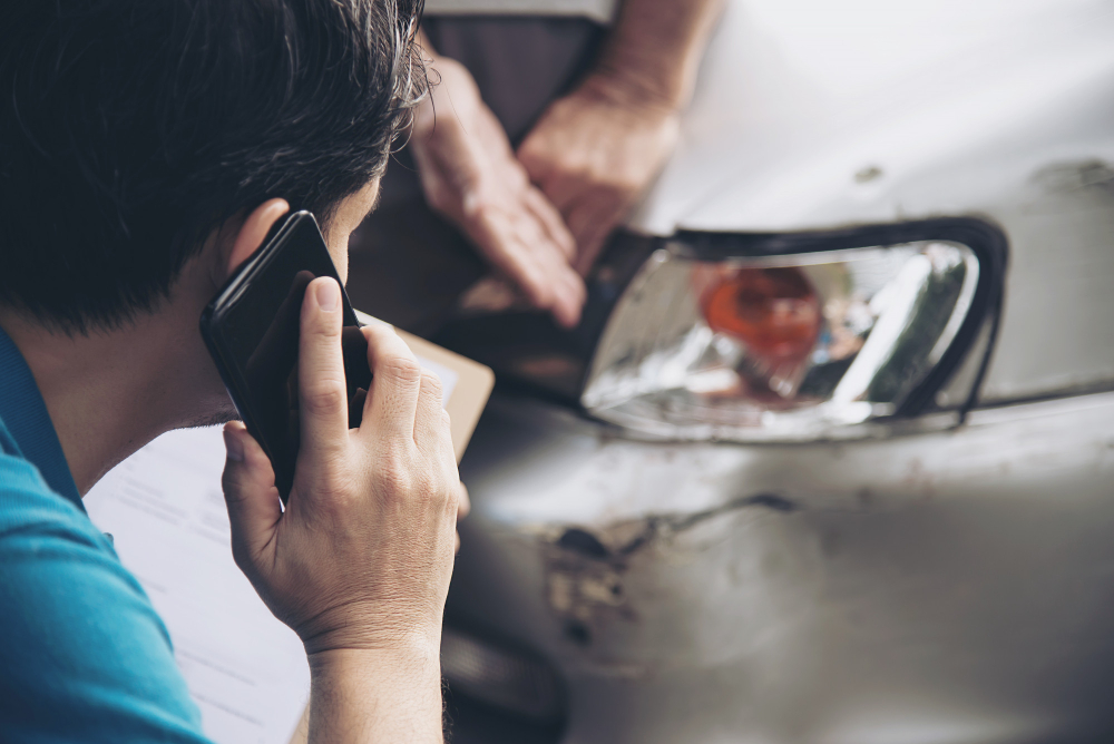 Homme au téléphone devant voiture accidentée au phare avant gauche